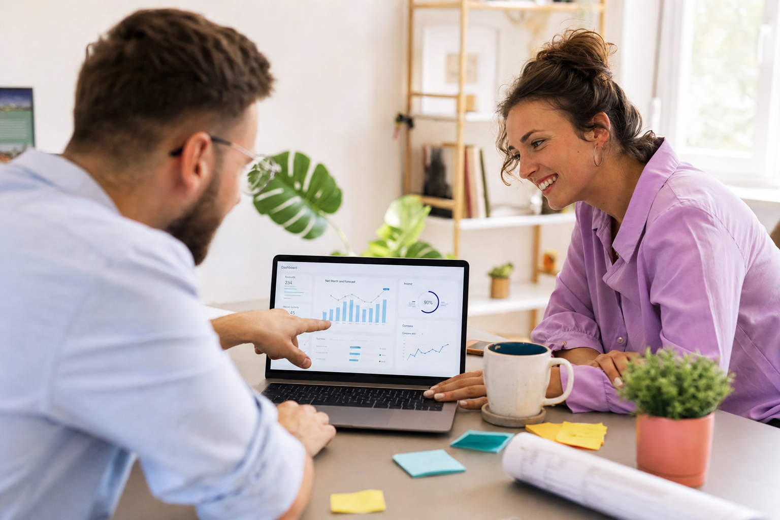 Twee collega’s bekijken samen grafieken en dashboards op een laptop aan een bureau.