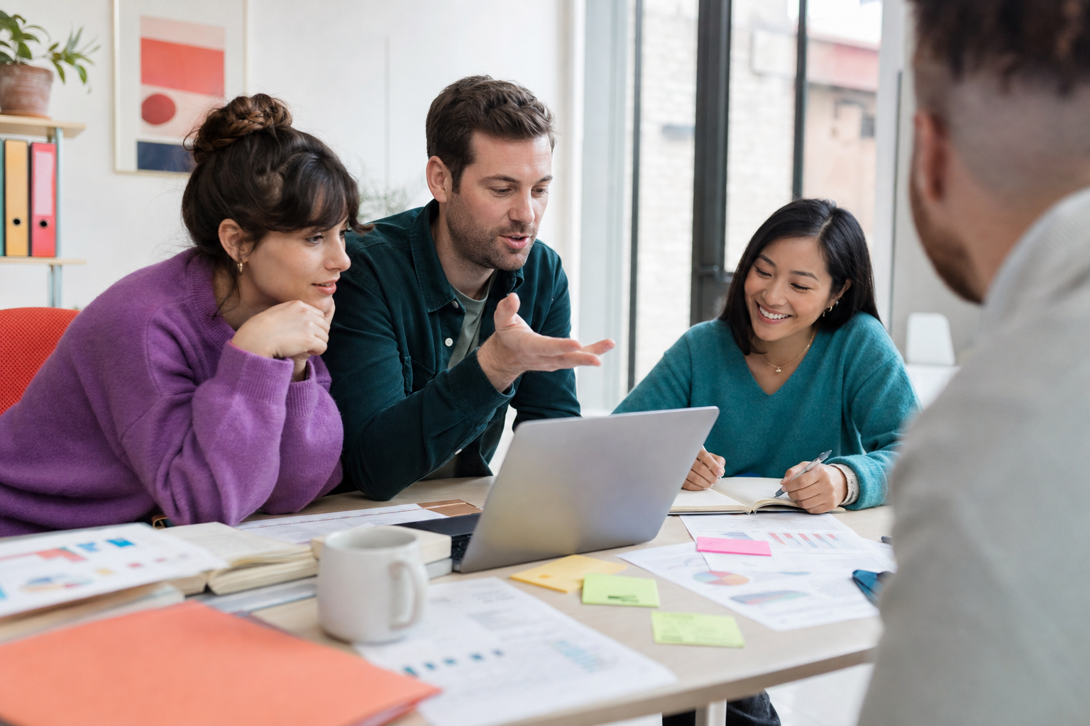 Drie collega’s overleggen aan tafel rond een laptop met notities, grafieken en kleurrijke post-its.